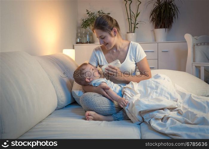 Portrait of young mother feeding her baby from bottle in bed at night