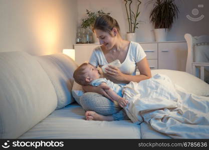 Portrait of young mother feeding her baby from bottle in bed at night