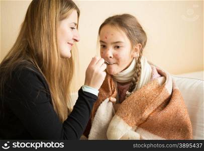 Portrait of young mother giving medicines on spoon to daughter caught flu