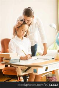 Portrait of young mother hugging and praising daughter while doing homework
