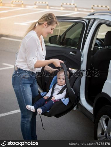Portrait of young mother installing car child seat with baby