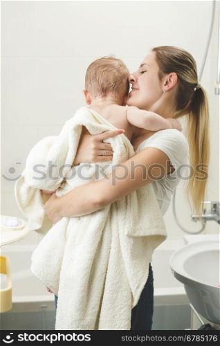Portrait of young mother kissing her baby at bathroom after having bath