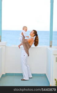 Portrait of young mother playing with baby on balcony with sea view&#xA;