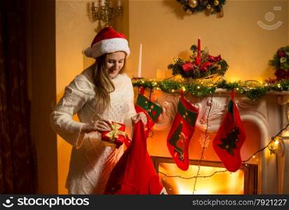 Portrait of young mother putting Christmas gifts in stockings hanging on fireplace