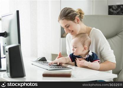 Portrait of young mother teaching her baby son using computer and typing on keyboard. Portrait of mother teaching her baby son using computer and typing on keyboard