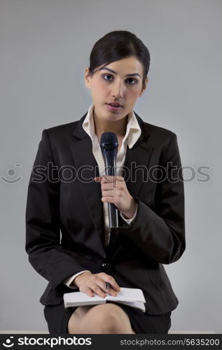 Portrait of young news reporter holding microphone with notepad