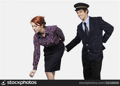 Portrait of young pilot touching flight attendant inappropriately against gray background