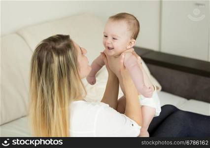 Portrait of young playful mother playing with her baby at bedroom