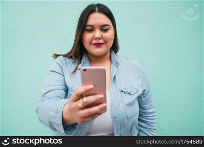 Portrait of young plus size woman doing video call on her mobile phone outdoors against light blue background. Communication concept.