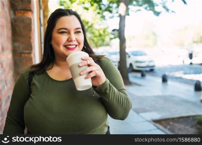 Portrait of young plus size woman holding a cup of coffee while walking outdoors. Urban concept.