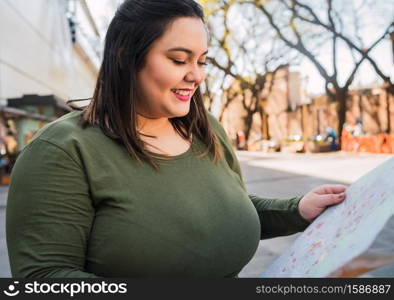 Portrait of young plus size woman holding a map and looking for directions outdoors in the street. Travel concept.