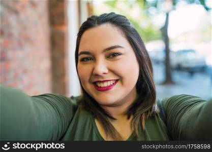 Portrait of young plus size woman smiling and taking a selfie outdoors at the street. Urban concept.