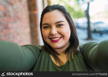 Portrait of young plus size woman smiling and taking a selfie outdoors at the street. Urban concept.