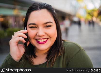 Portrait of young plus size woman smiling while talking on the phone outdoors at the street. Urban concept.