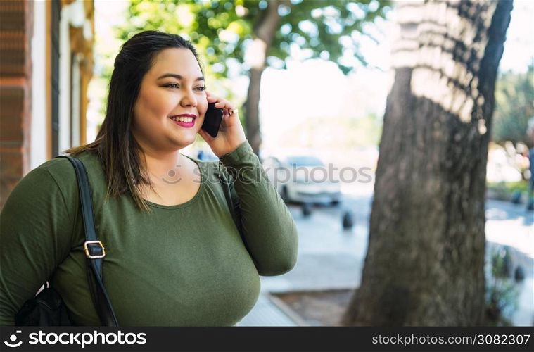 Portrait of young plus size woman smiling while talking on the phone outdoors at the street. Urban concept.
