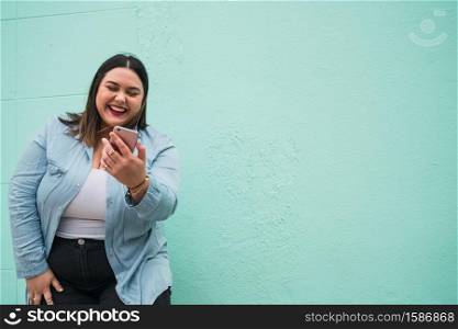Portrait of young plus size woman smiling while typing text message on her mobile phone outdoors. Technology concept.