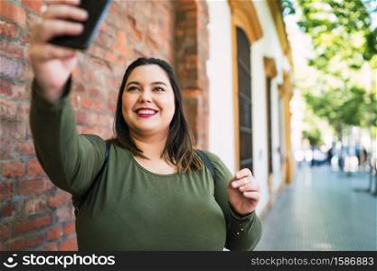 Portrait of young plus size woman taking selfies with her mophile phone outdoors at the street. Urban concept.