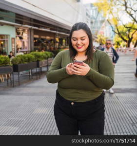 Portrait of young plus size woman typing text message on her mobile phone outdoors at the sreet. Technology concept.