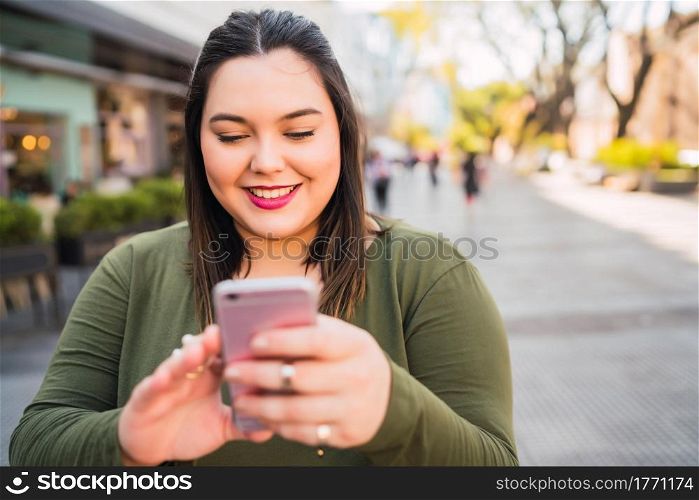Portrait of young plus size woman typing text message on her mobile phone outdoors at the sreet. Technology concept.