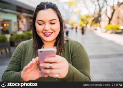 Portrait of young plus size woman typing text message on her mobile phone outdoors at the sreet. Technology concept.
