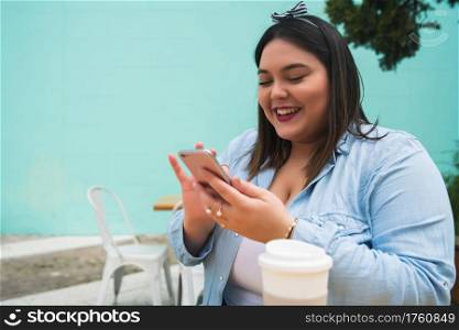 Portrait of young plus size woman using her mobile phone while sitting at coffee shop. Communication and technology concept.