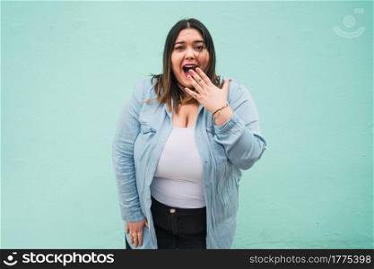 Portrait of young pluse size woman with a shocked expression while standing against light blue wall outdoors.