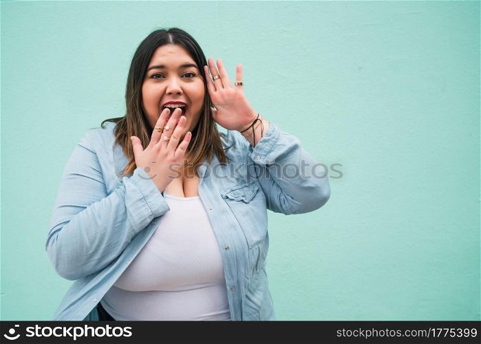 Portrait of young pluse size woman with a shocked expression while standing against light blue wall outdoors.