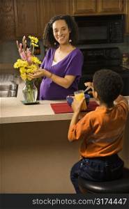 Portrait of young pregnant mother arranging flowers while son eats breakfast.