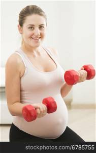 Portrait of young pregnant woman exercising with weights at home