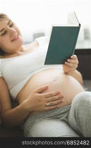 Portrait of young pregnant woman reading book on sofa
