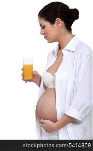 portrait of young pregnant woman standing with glass of orange juice and hand on belly