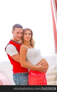Portrait of young pregnant woman with husband hugging her tummy&#xA;