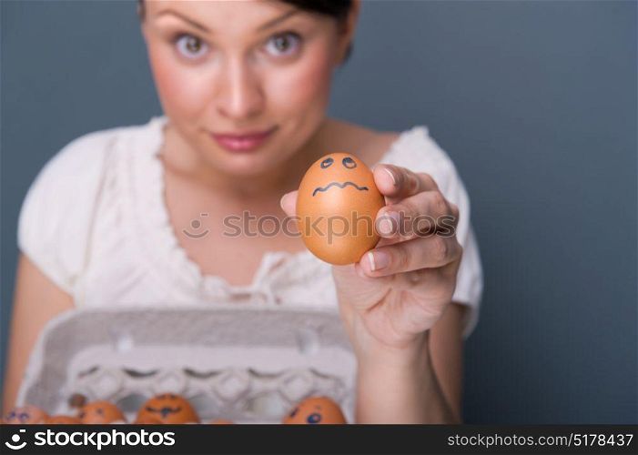 Portrait of young pretty business woman against grey background holding eggs with different emotions on their rawn faces. People management conceptual photo.