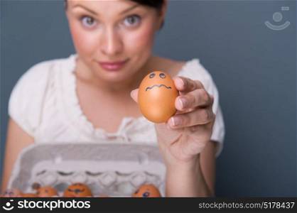 Portrait of young pretty business woman against grey background holding eggs with different emotions on their rawn faces. People management conceptual photo.