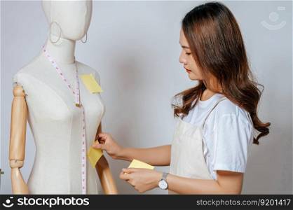 Portrait of young pretty female fashion designer stylish smile and take a note, Tailor woman&rsquo;s taking note after measurements with measuring tape on mannequin in studio at home