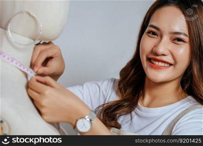 Portrait of young pretty female fashion designer stylish smile during working at fashion studio, Tailor woman’s taking measurements with measuring tape on mannequin in studio at home