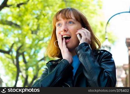 Portrait of young redhead woman talking on her mobile phone. Outdoors.