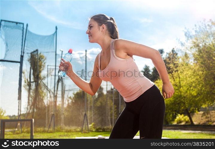 Portrait of young running woman with bottle of water on stadium
