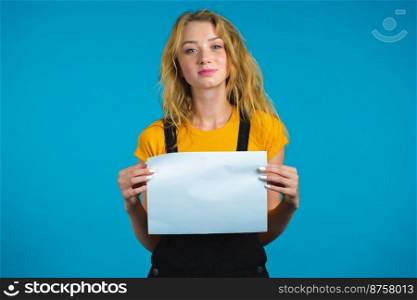 Portrait of young serious woman holding white a4 paper isolated on blue studio background.Copy space. Portrait of young serious woman holding white a4 paper isolated on blue studio background.Copy space.