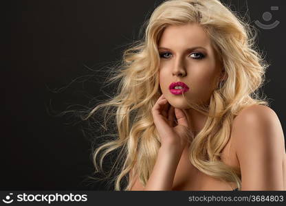 portrait of young sexy girl with blode wavy hairstyle and and flying hair from wind, she is turned of three quarters, looks in to the lens and her right hand is near the face