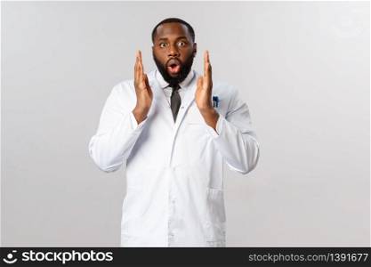 Portrait of young shocked speechless african-american male doctor, physician heard laboratory starts testing covid-19 vaccine, feel astounded and amazed, staring camera startled, grey background.. Portrait of young shocked speechless african-american male doctor, physician heard laboratory starts testing covid-19 vaccine, feel astounded and amazed, staring camera startled, grey background