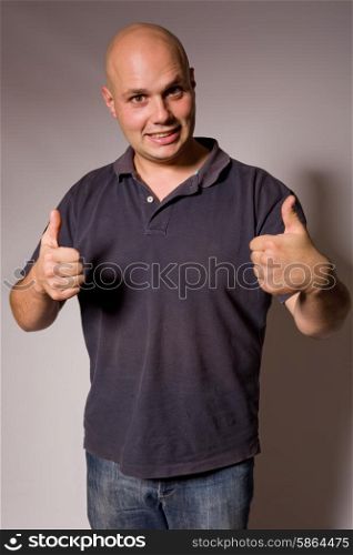 Portrait of young silly man going thumbs up, on a dark background