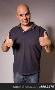 Portrait of young silly man going thumbs up, on a dark background