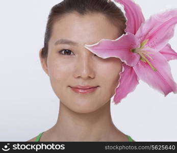 Portrait of young, smiling, beautiful woman with a large pink flower tucked behind her ear, studio shot