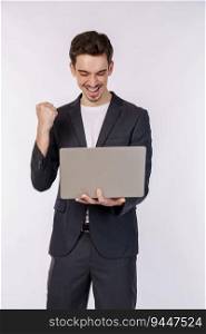 Portrait of young smiling businessman holding laptop in hands, typing and browsing web pages while doing a winning closed fist gesture isolated on white background. Technology, business concept.