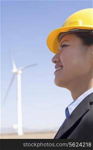 Portrait of young smiling female engineer checking wind turbines on site, side view