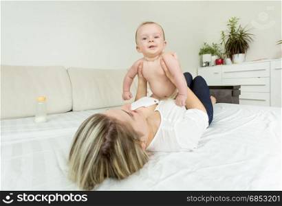Portrait of young smiling woman playing with baby on bed