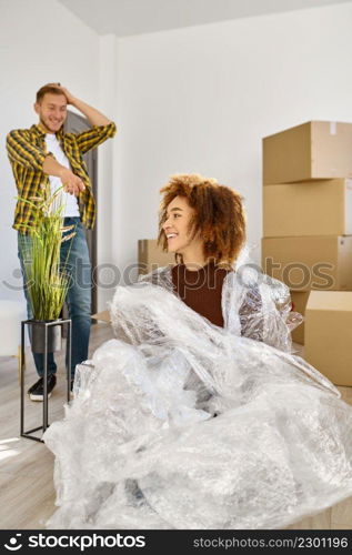 Portrait of young smiling woman wrapped in packing bubble tape fooling around during home moving. Woman wrapped in packing bubble tape portrait