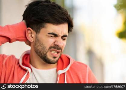 Portrait of young stressed man suffering headache outdoors on the street.