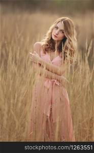 portrait of young stylish woman in field in grass. blond girl with make up and long hair in a pink dress.. portrait of young stylish woman in field in grass. blond girl with make up and long hair in a pink dress